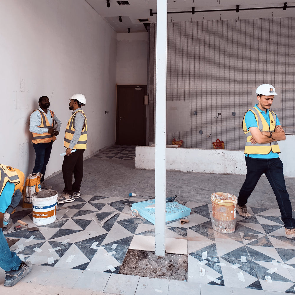 Workers in a room with tiled floors and walls, one holding a bucket.