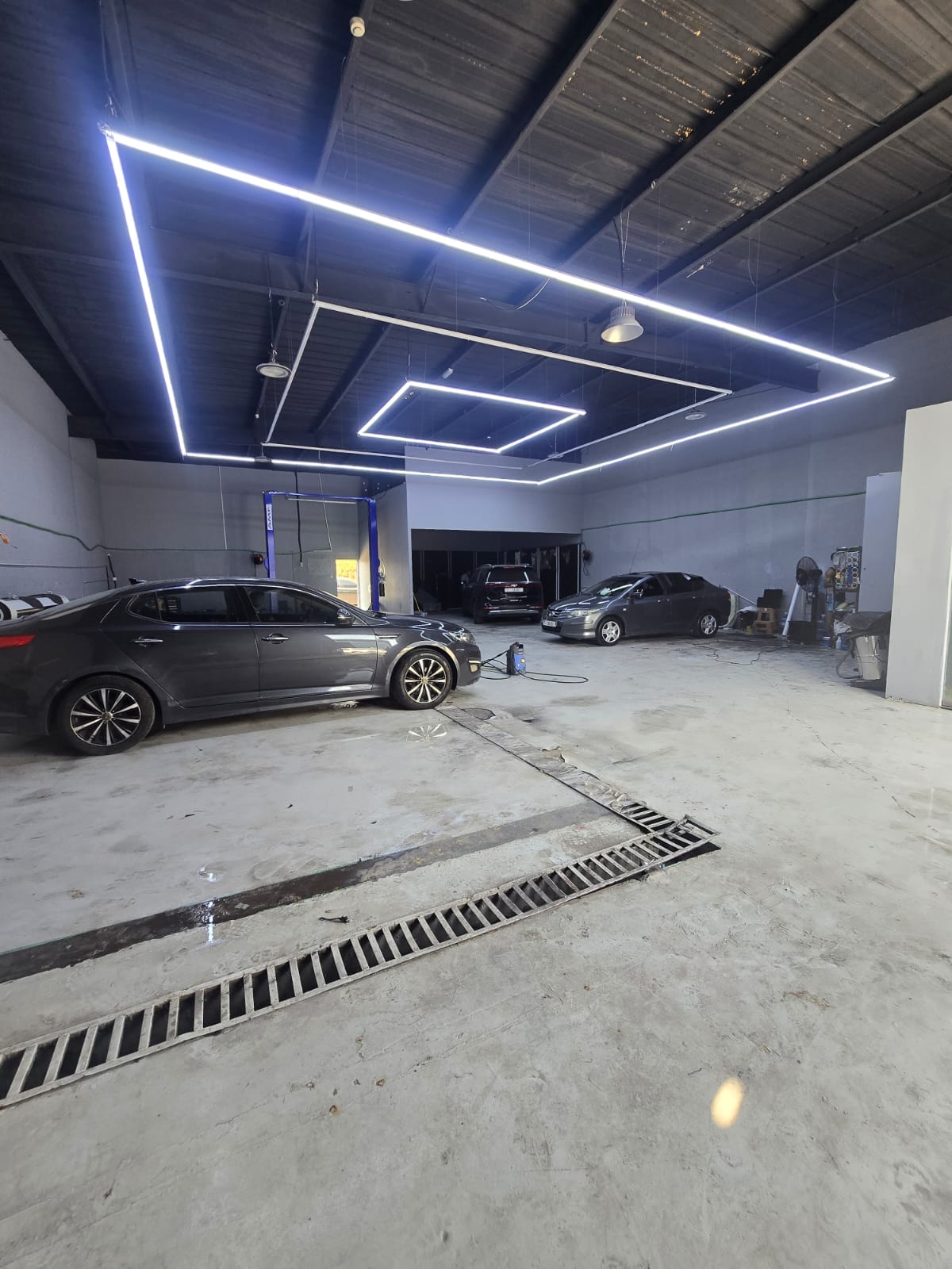 Modern car showroom with cars on display under a ceiling with embedded lighting fixtures.