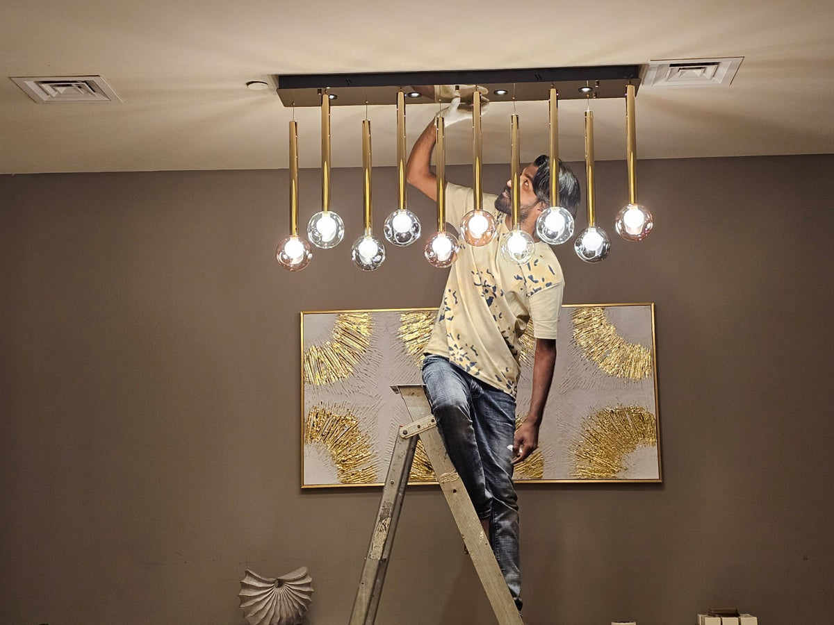 Person installing a chandelier on a ladder with a decorative wall painting in the background.