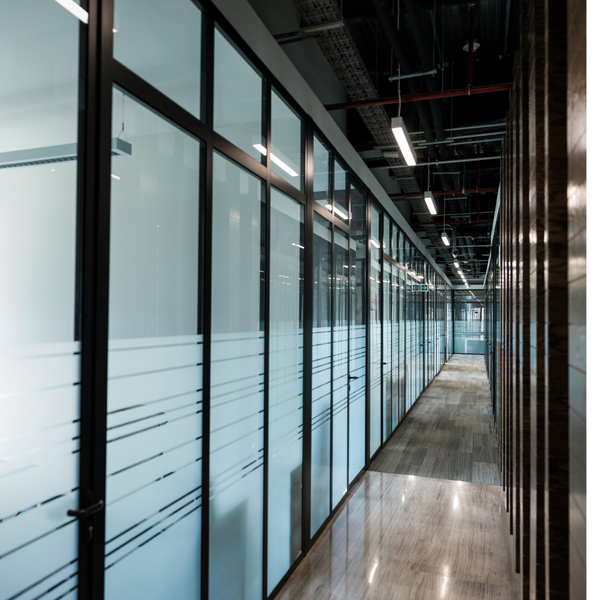 Long corridor with glass-walled office cubicles in a modern building.