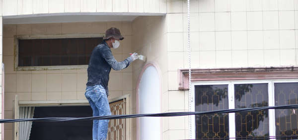 Person painting a building exterior with a ladder and safety harness.