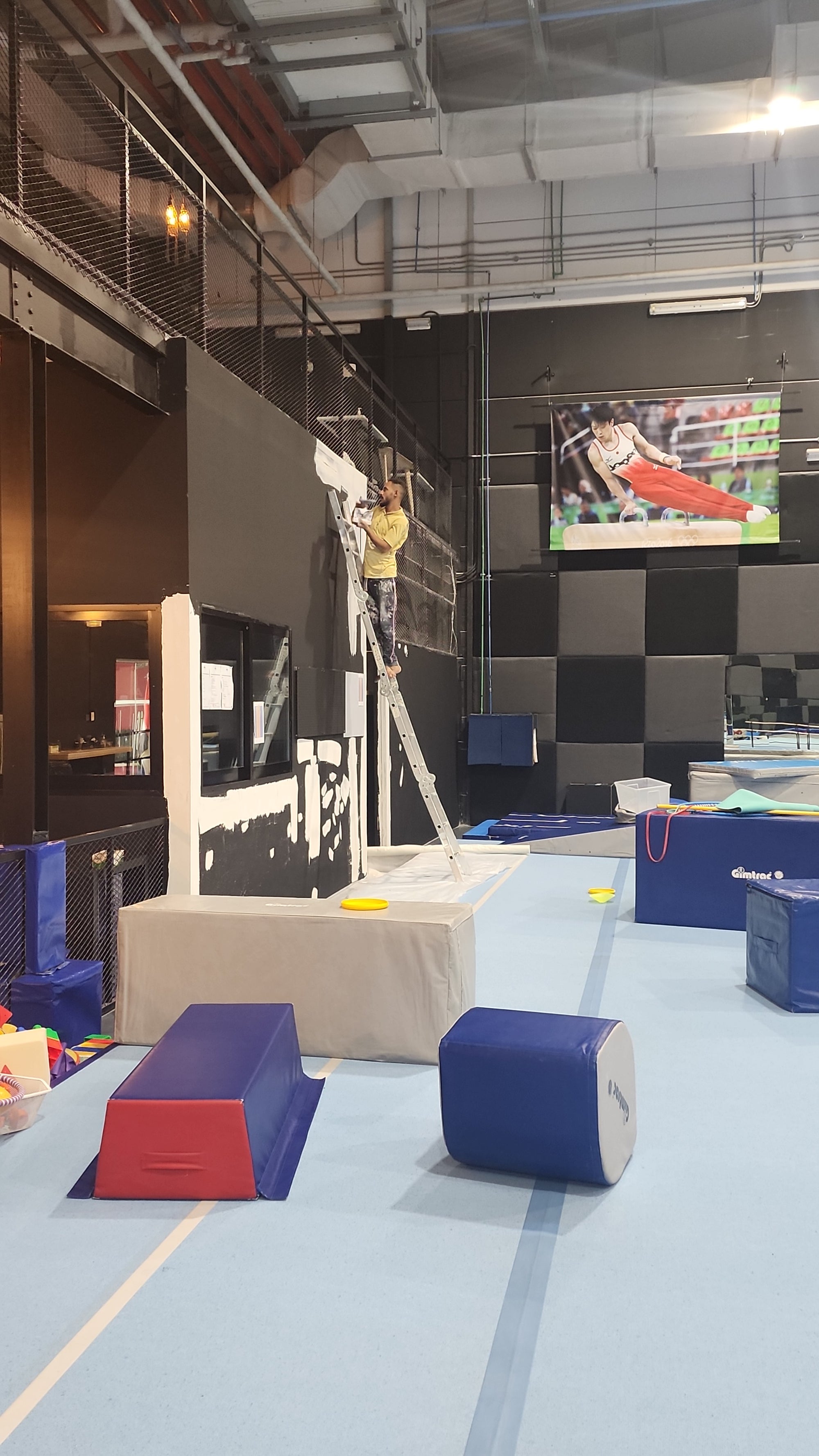 An indoor play area or gymnasium with a large black-and-white painted target on the floor, blue padded wall blocks, and a light blue wall. No person is clearly visible in a way that would make this a lifestyle shot; it reads as an environmental or facility view.