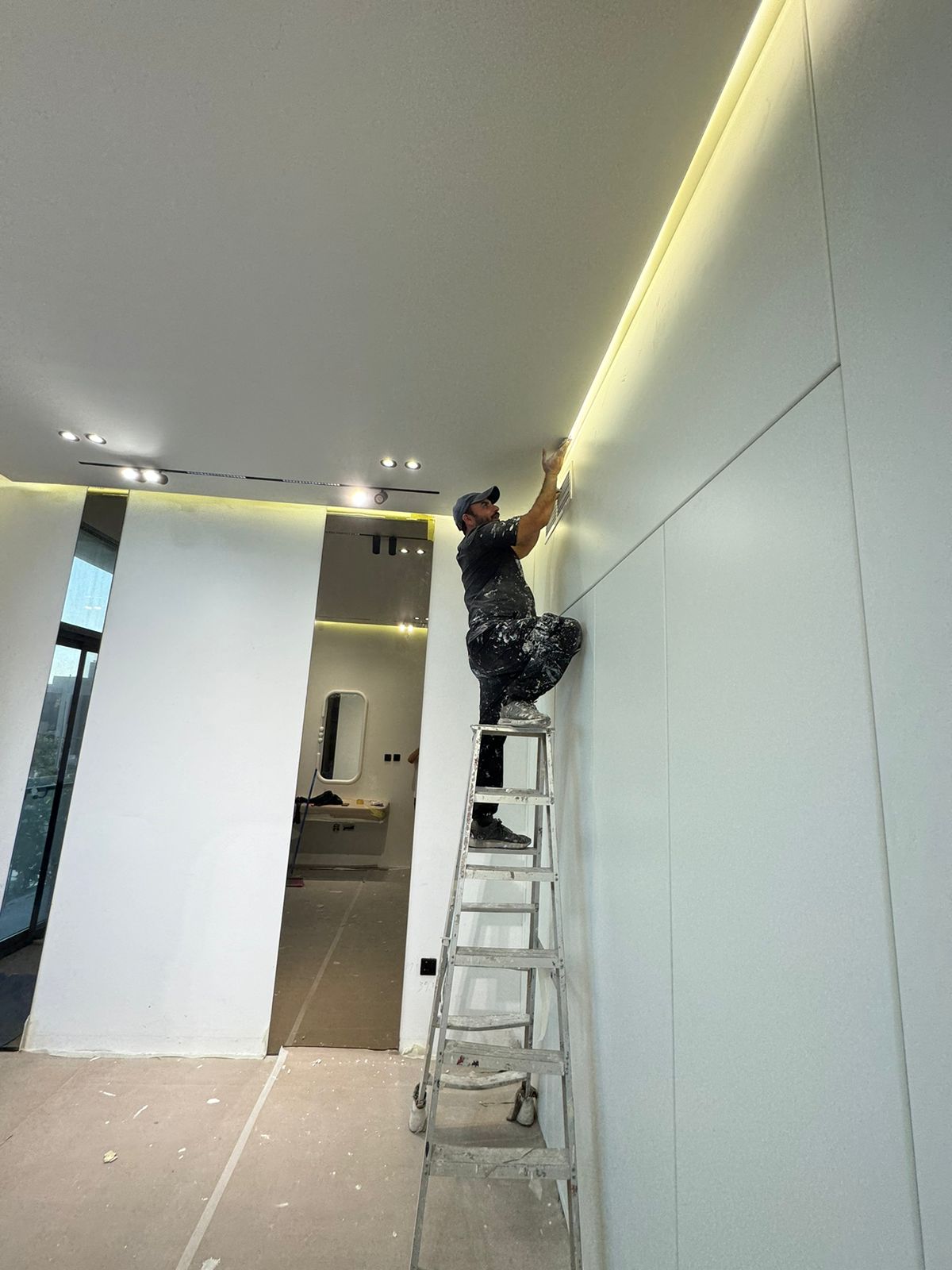 Person on a ladder painting a wall in a modern interior setting