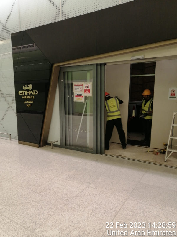 Two workers in high-visibility vests and hard hats near a glass door with Etihad Airways branding.